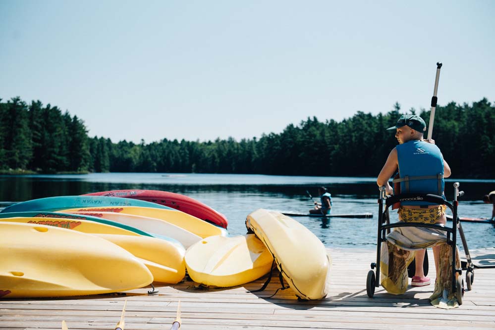 camper in wheelchair on dock at camp next to kayaks