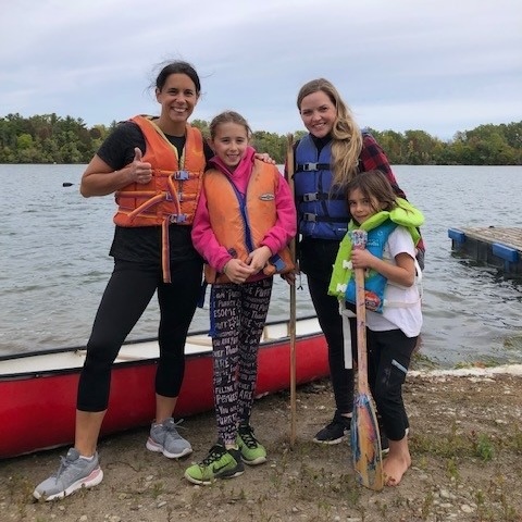 family in lifejackets with canoe and lake in background