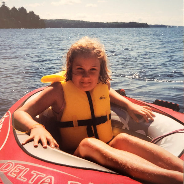 camper wearing a life jacket in an inner tube on the lake with trees and clear skies in the background