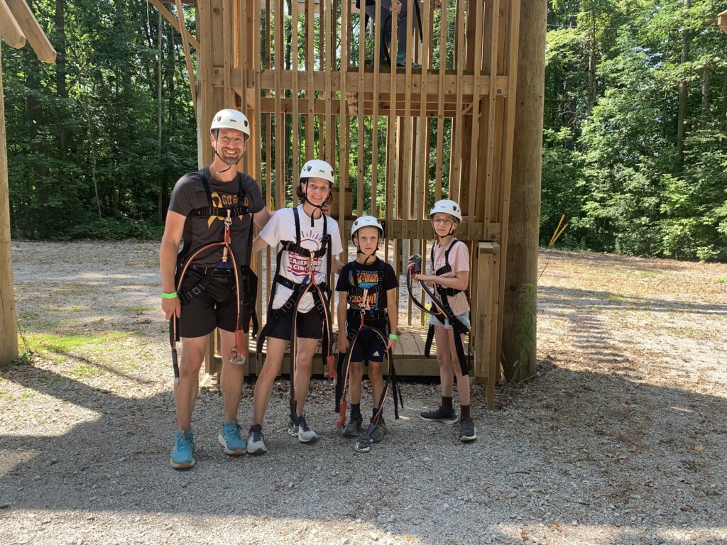 emma and family at the climbing wall at camp, in safety gear