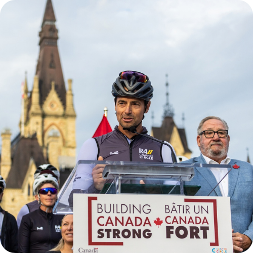 adam van koeverden and chris malette speaking on parliament hill with riders in the background
