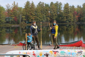 child in wheelchair on dock at camp with parents