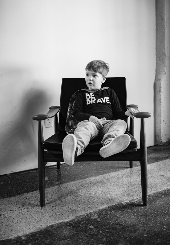 benjamin sitting in a chair, wearing a shirt that says be brave