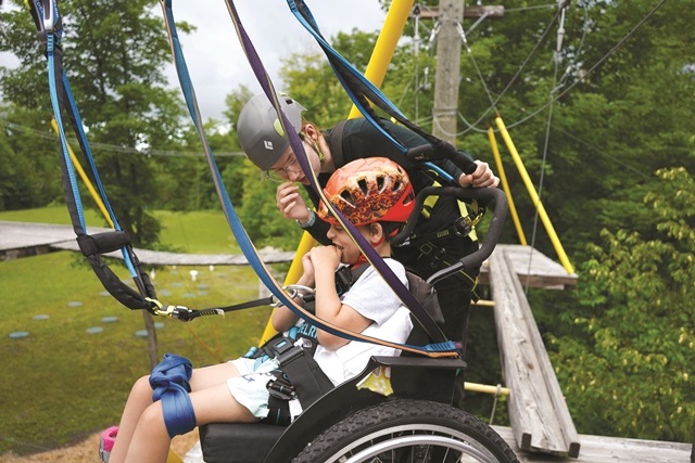 noah on the accessible high ropes course at camp, with volunteer by his side