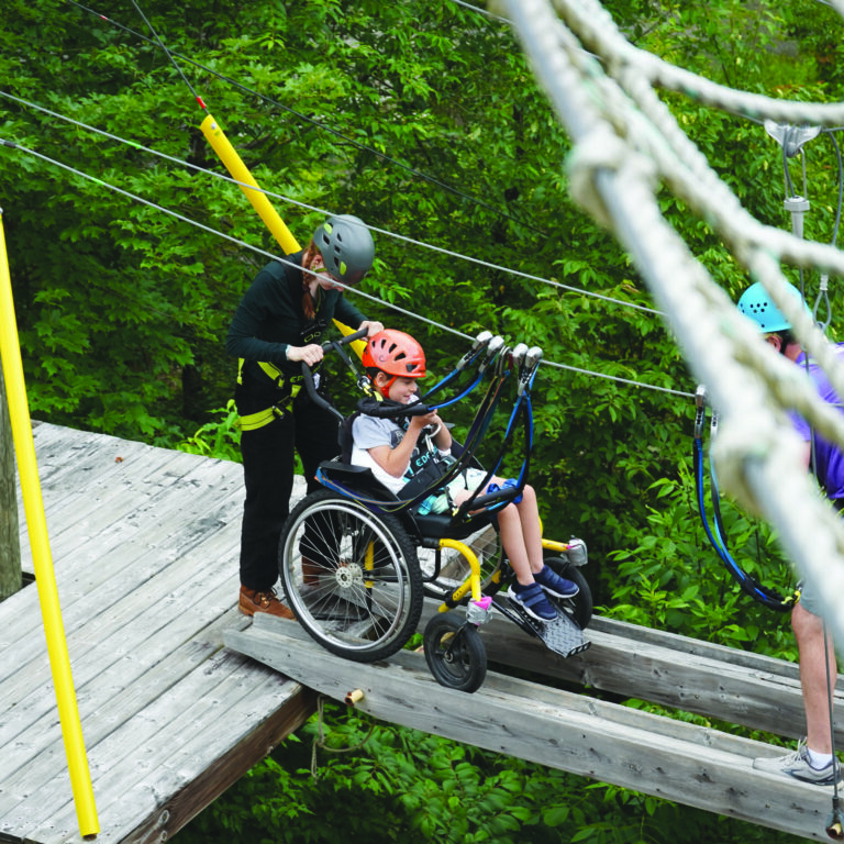noah on the accessible high ropes course at camp with a volunteer by his side