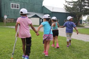Camper with leg brace and crutch holding hands with other camper walking through grass