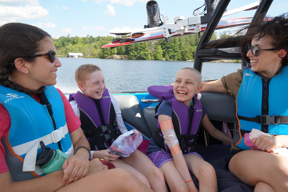 Two campers in life jackets laughing with volunteers on boat in the lake