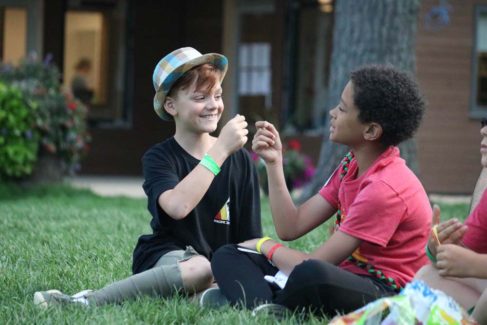 Two campers sitting on the grass playing rock, paper, scissors