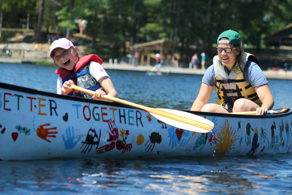 Laughing camper on canoe with volunteer in the lake at CAMPFIRE CIRCLE Muskoka