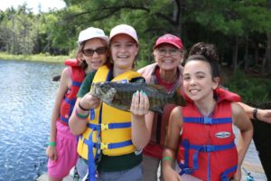 Three campers and volunteer holding up large fish they caught on fishing dock of Lake Donner