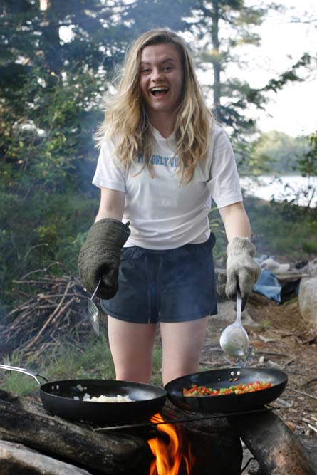 Smiling camper cooking meal on the camp fire