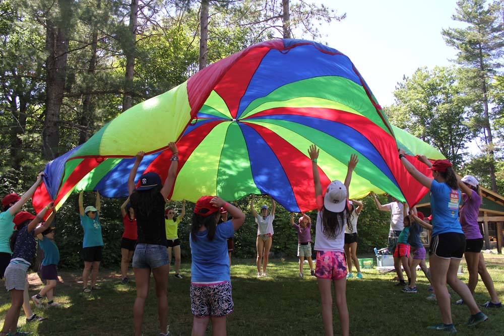 Campers and volunteers playing with parachute in the grass at CAMPFIRE CIRCLE Muskoka