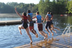 Rentals at camp. Five campers jumping off dock into the lake at Campfire Circle Muskoka.