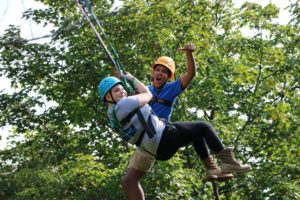 Two campers hanging from giant swing in forest at CAMPFIRE CIRCLE Muskoka
