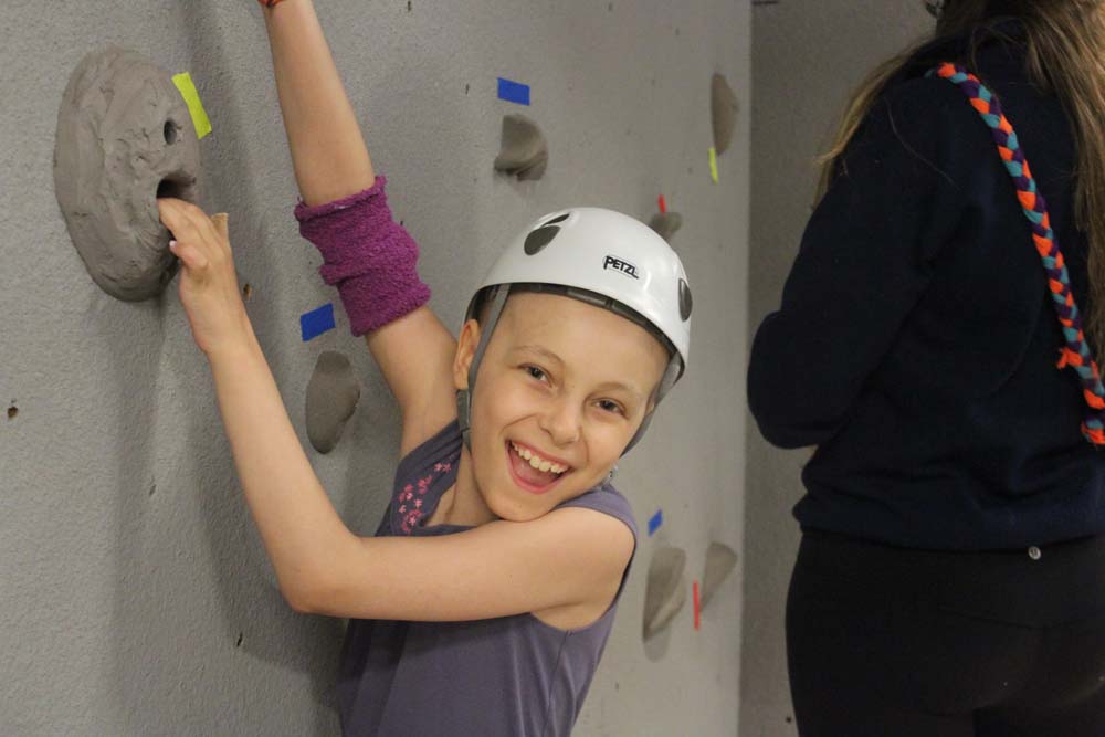 Smiling camper hanging from rock wall wearing helmet