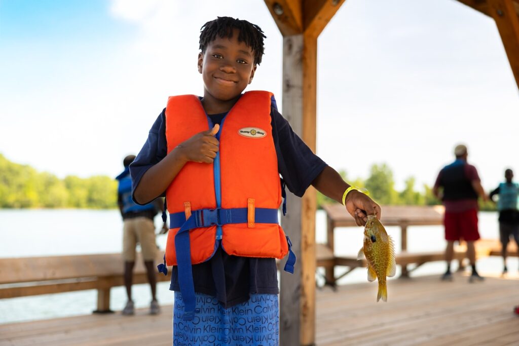 camper wearing lifejacket holding a fish that he caught