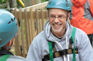 Dr. Malkin in adventure gear smiling at camper on adventure course