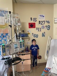 emerson in a blue jays jersey standing next to a wall in his hospital room