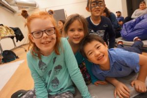 Smiling campers sitting on floor of gym at CAMPFIRE CIRCLE Downtown