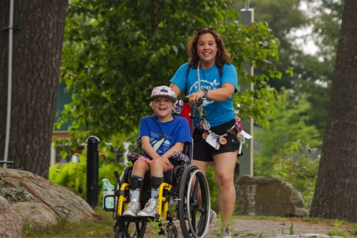 volunteer pushing camper in a wheelchair at camp