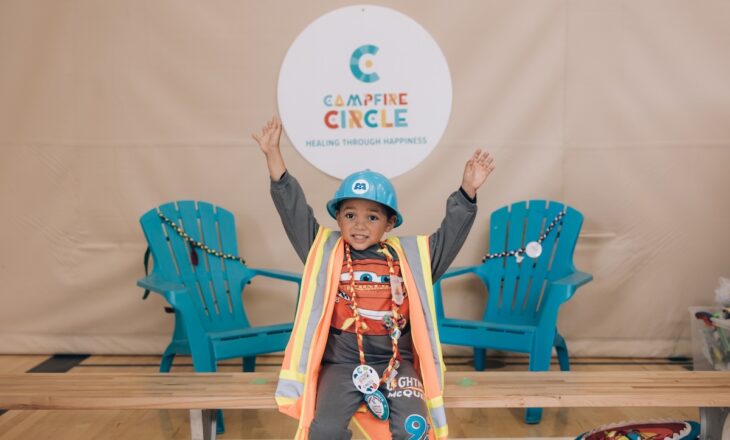 carter wearing construction costume in front of chairs and campfire circle sign at camp