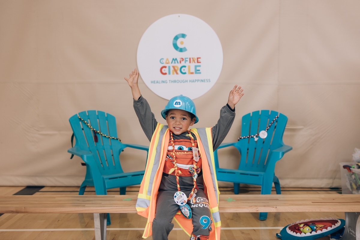 carter wearing construction costume in front of chairs and campfire circle sign at camp