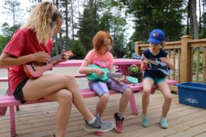 campers playing ukulele with counselor on picnic table at camp