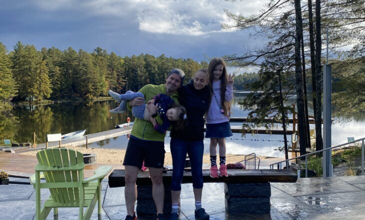 family picture at camp with lake and trees in background