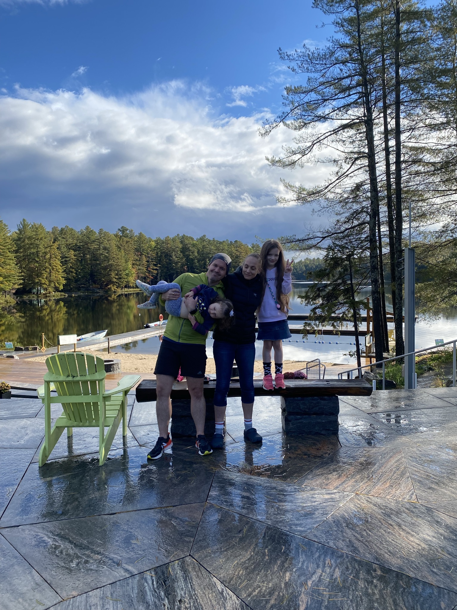 family standing in front of the water at camp in muskoka with trees in background