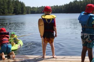 campers in lifejackets and hats on the dock standing towards the lake at camp