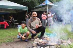 child and father around a campfire surrounded by other families at a family camping trip
