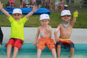 three campers sitting with feet in kiddie pool, smiling at day camp