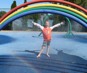 camper standing in a splash pad with a rainbow over them