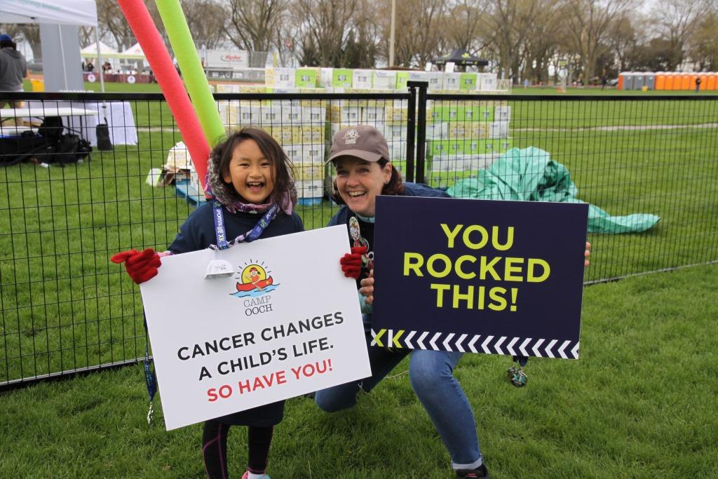 Volunteer with camper holding up cheer signs on grass at SL10K event