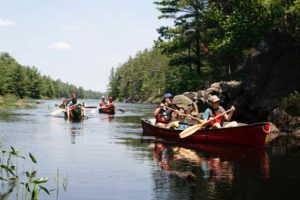 three canoes on a lake with campers surrounded by trees and rocks