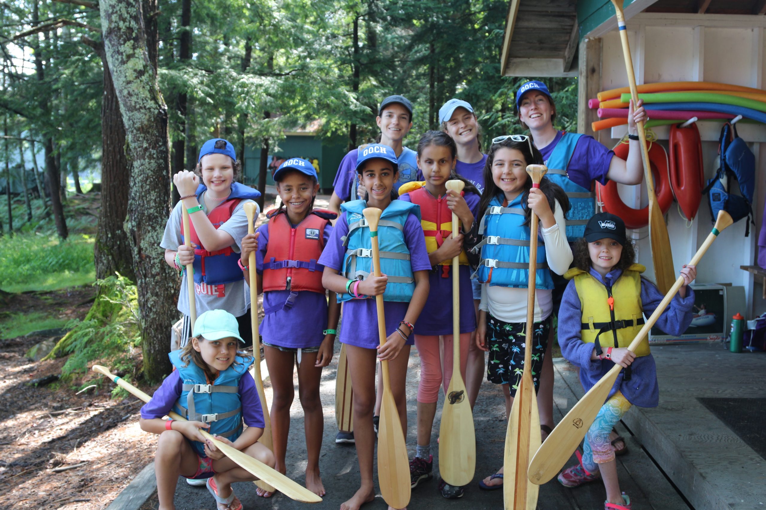 group of campers together in lifejackets with canoe paddles at camp