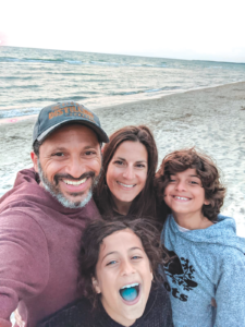 family standing together outside, smiling on the beach