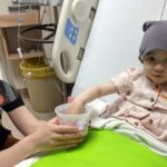 Elliana with her hand in a cup sitting in a hospital bed