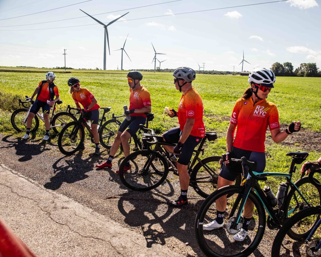 group of riders on the side of the road for a food break with windmills and clear sky in the background