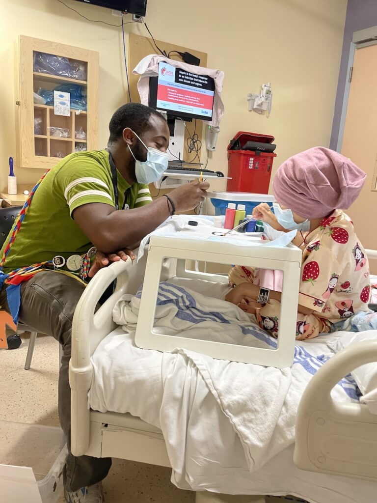radda in hospital bed with campfire circle staff doing arts and crafts