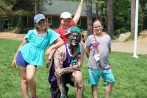 counselor covered in paint with smiling campers outside at camp