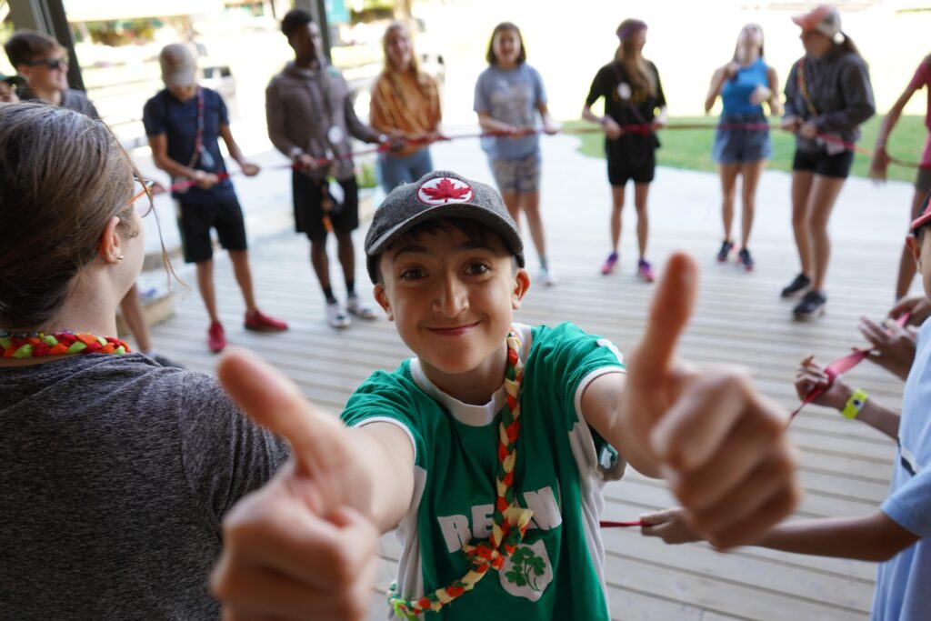 camper giving thumbs up to the camera with other campers in the background
