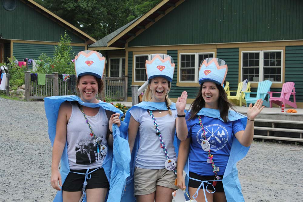 Nurses in queen costumes waving and smiling on the gravel in front of cabin