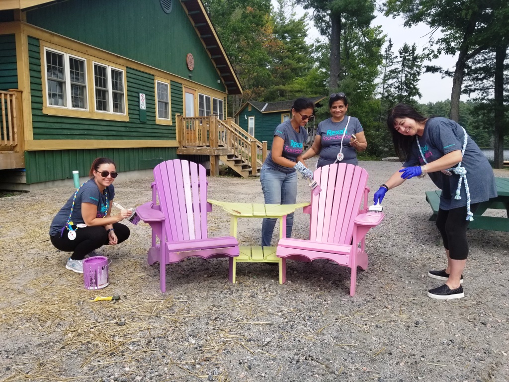 Corporate volunteers painting new patio chairs outside at Ooch Muskoka